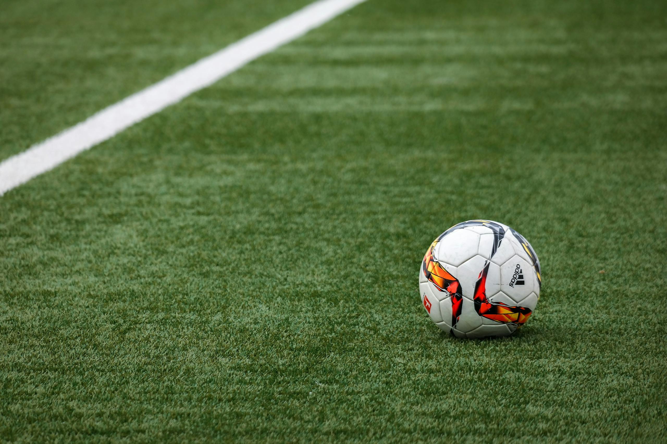 Ein leuchtender Fußball liegt auf einem makellosen Rasen neben einer weißen Seitenlinie.