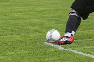 Dynamische Aufnahme eines Fußballspielers, der auf einem Rasenfeld den Ball kickt und dabei rasante Sportaktion zeigt.