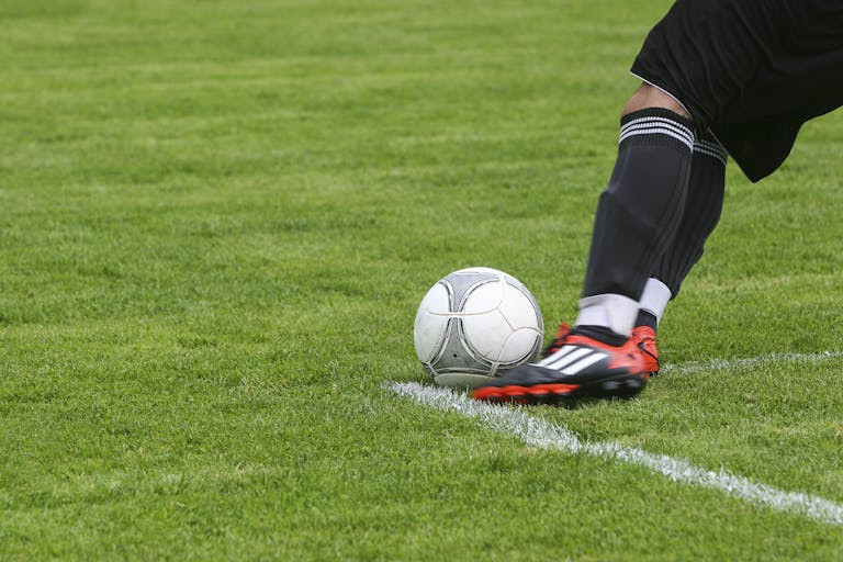 Dynamische Aufnahme eines Fußballspielers, der auf einem Rasenfeld den Ball kickt und dabei rasante Sportaktion zeigt.