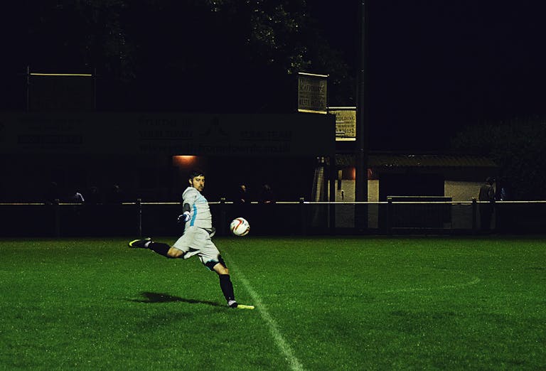 Dynamische Actionaufnahme eines Fußballspielers, der während eines Nachtmatches in Somerset, England, den Ball schießt.
