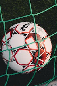 Nahaufnahme eines Fußballs, der in einem Netz auf einem Rasenfeld gefangen ist, ideal für Sportmotive.
