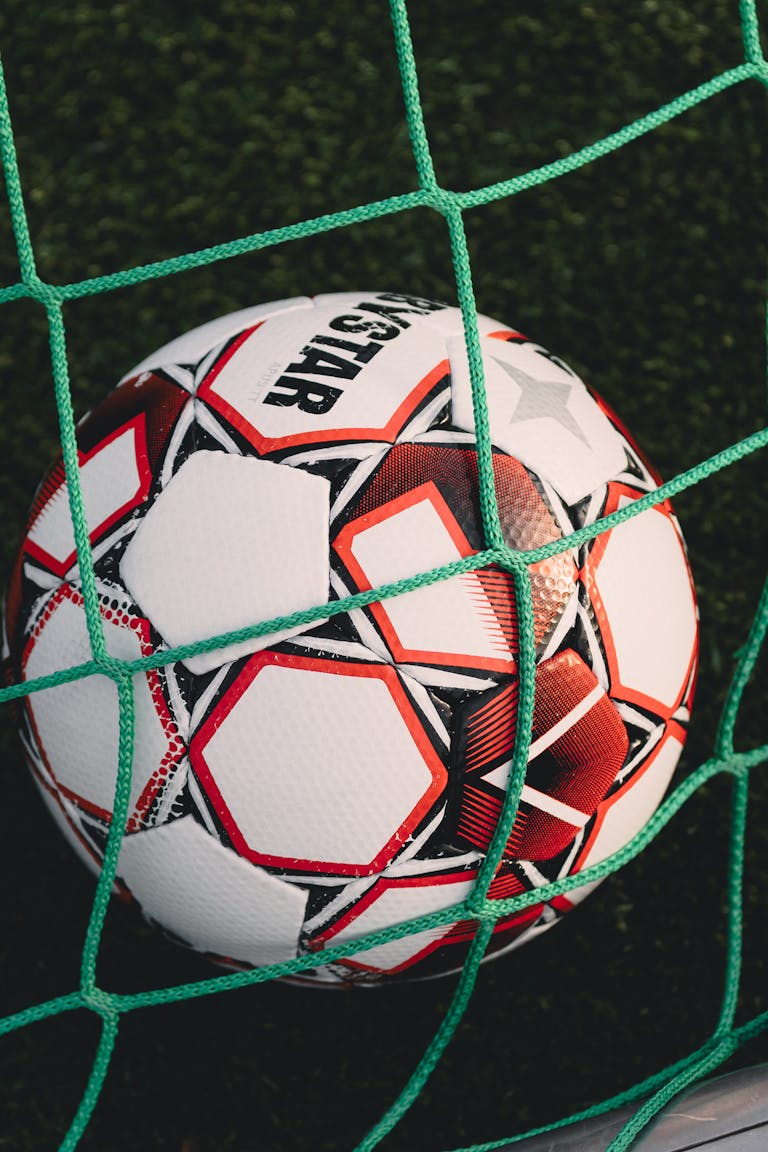 Nahaufnahme eines Fußballs, der in einem Netz auf einem Rasenfeld gefangen ist, ideal für Sportmotive.