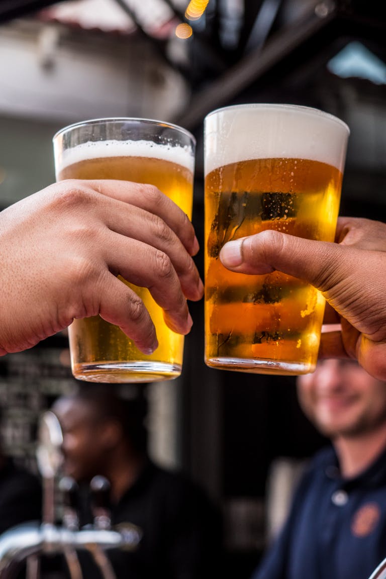 Nahaufnahme zweier Freunde, die in einer lebhaften Bar mit kalten Biergläsern anstoßen und ihre Freundschaft und die schönen Zeiten feiern.