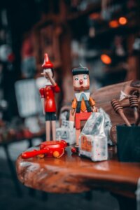 Holzpuppen von Pinocchio und kleine Spielzeugfahrzeuge, ausgestellt auf einer Holzoberfläche mit unscharfem Hintergrund.