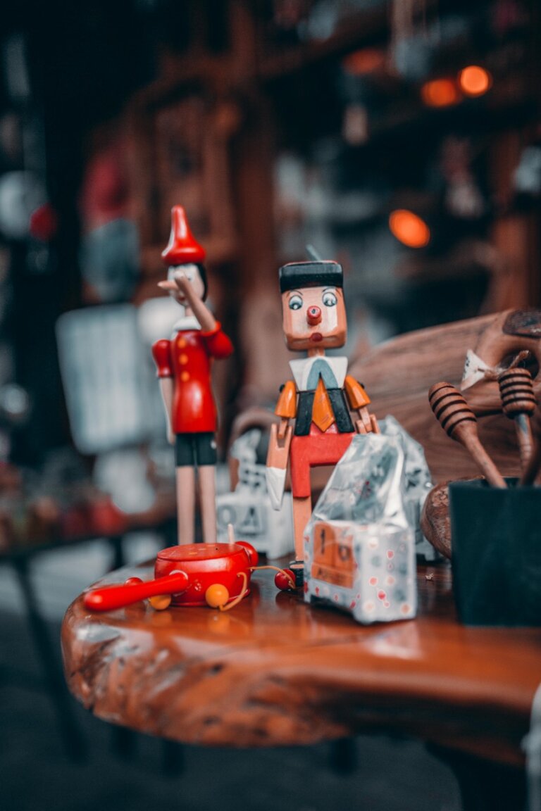Holzpuppen von Pinocchio und kleine Spielzeugfahrzeuge, ausgestellt auf einer Holzoberfläche mit unscharfem Hintergrund.